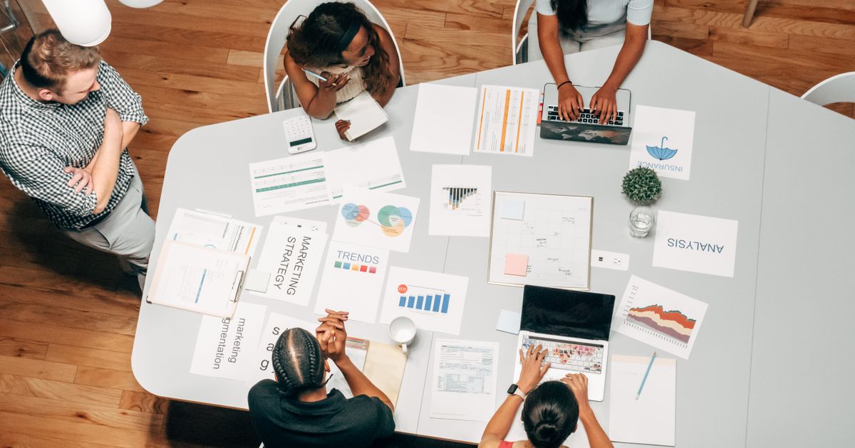 Equipe reunida ao redor de mesa com relatórios impressos e gráficos coloridos