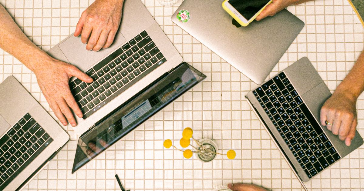 Vista de cima de uma mesa com dois notebooks, celular e anotações durante reunião