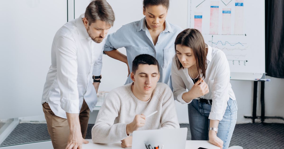 Equipe em pé analisando gráficos junto a um colega no notebook