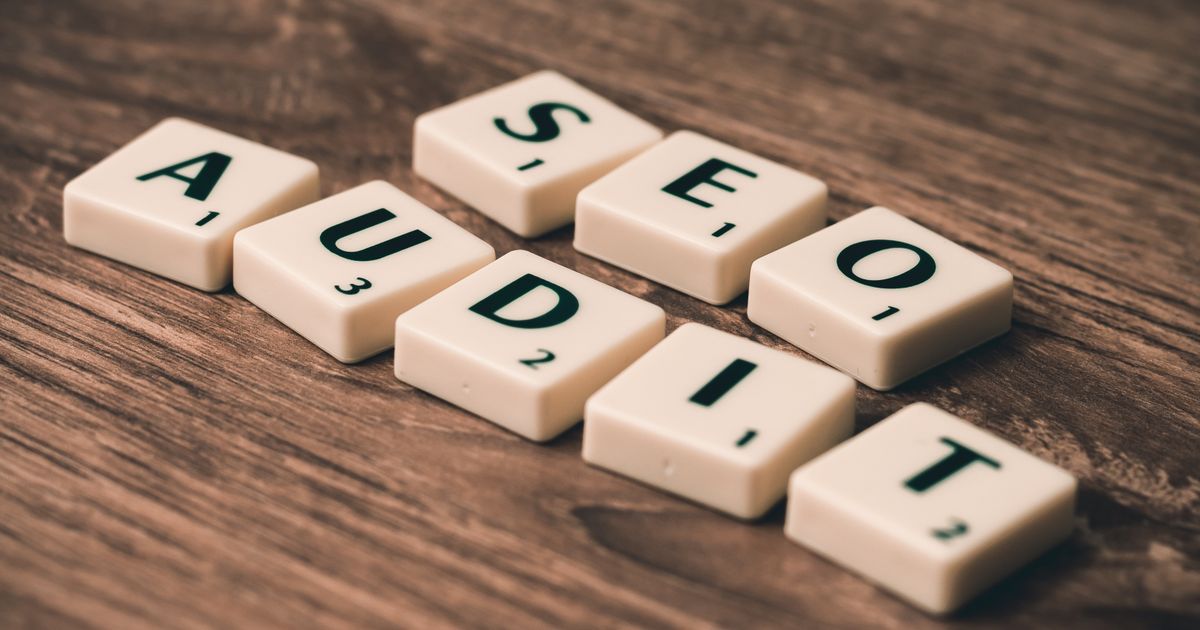Peças de jogo de palavras formando SEO AUDIT sobre mesa de madeira