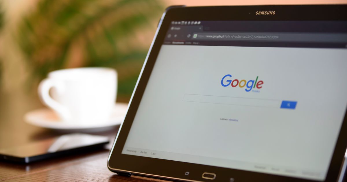 Tablet exibindo a busca do Google sobre a mesa, com xícara de café ao fundo