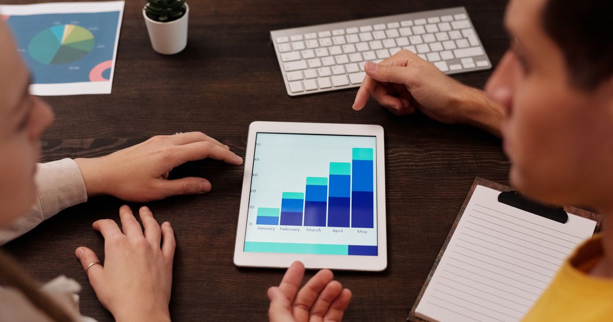 Mãos apontando para gráfico em tablet sobre mesa com teclado e bloco de notas