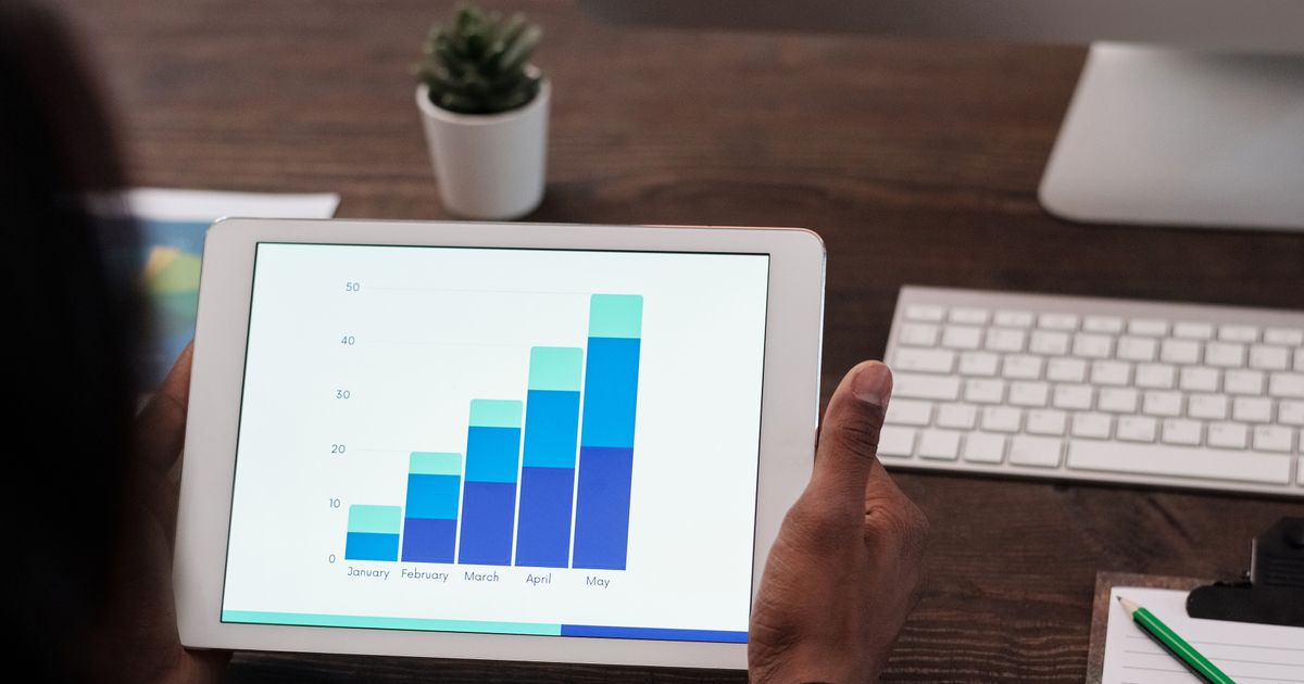Mãos segurando tablet com gráfico de barras crescente sobre mesa de escritório