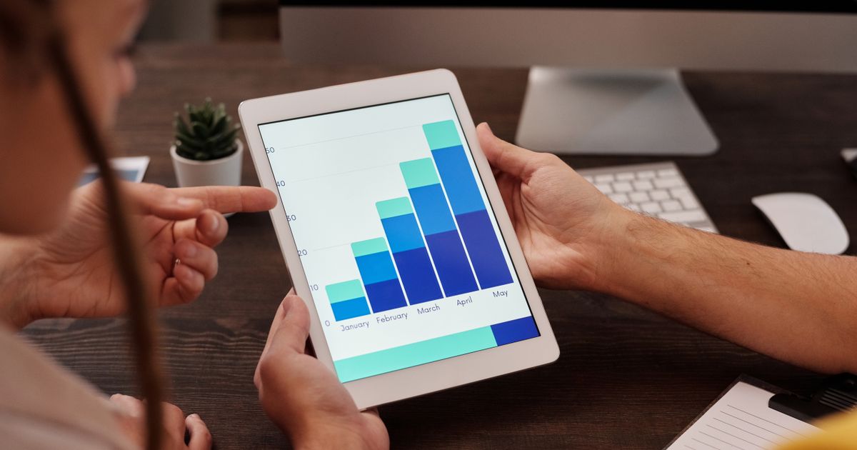 Duas pessoas analisando um gráfico de barras num tablet durante reunião