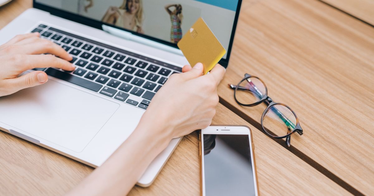 Mãos digitando em notebook com cartão em mãos, finalizando uma compra online