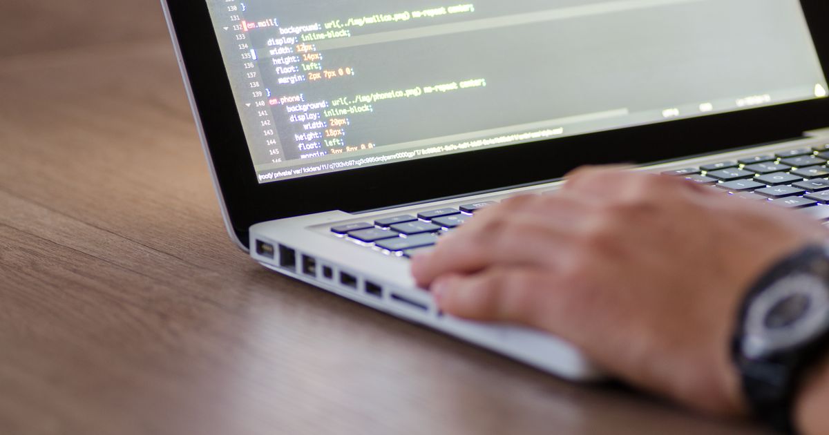 Mãos digitando em notebook com código de programação na tela