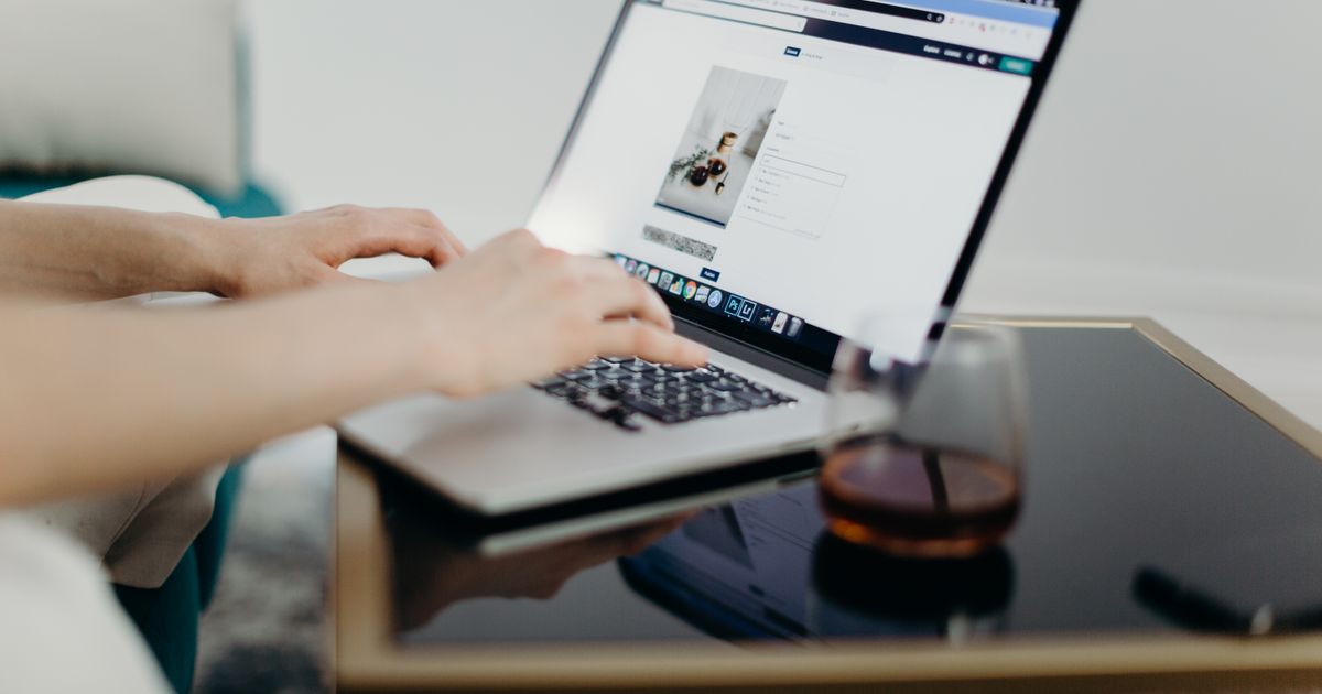 Mãos digitando em notebook exibindo um site, sobre mesa de madeira