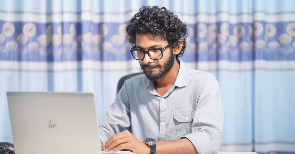 Homem de óculos sorrindo enquanto trabalha em um notebook, em ambiente iluminado